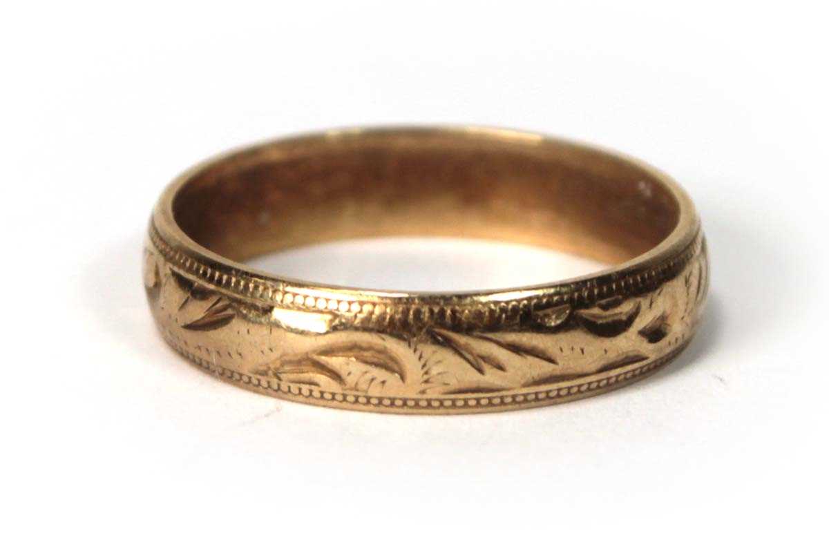 Lot 533 - A 9ct yellow gold scroll engraved wedding band,...