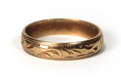 Lot 533 - A 9ct yellow gold scroll engraved wedding band,...