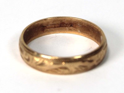 Lot 533 - A 9ct yellow gold scroll engraved wedding band,...