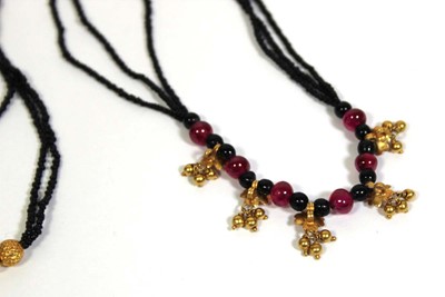 Lot 712 - A triple strand black bead necklace suspending...